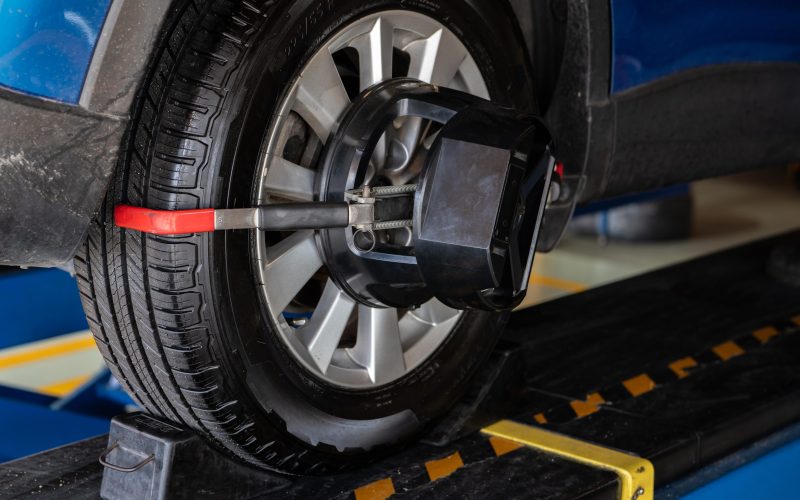 Wheel alignment equipment grip the tire of car wheel in car repair shop. Auto wheel alignment in workshop of service station. Car wheel balance. Suspension adjustment. Vehicle inside garage workshop.